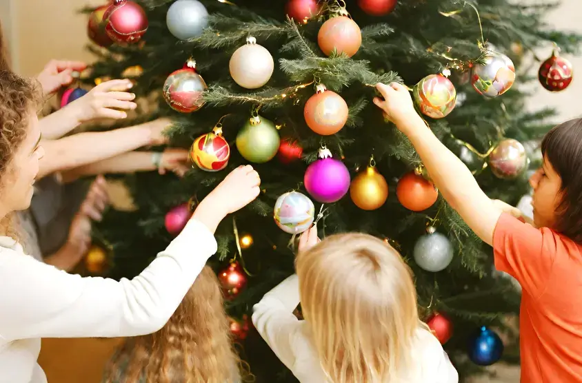 Dzieci wesoło dekorujące choinkę, atrakcja podczas pakietów bożonarodzeniowych w górach.